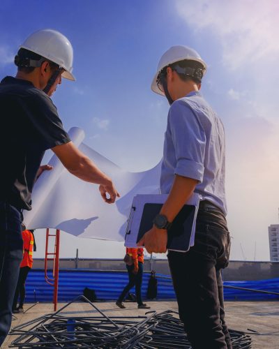 Structural engineer and architect working with blueprints discuss at the outdoors building construction site.
